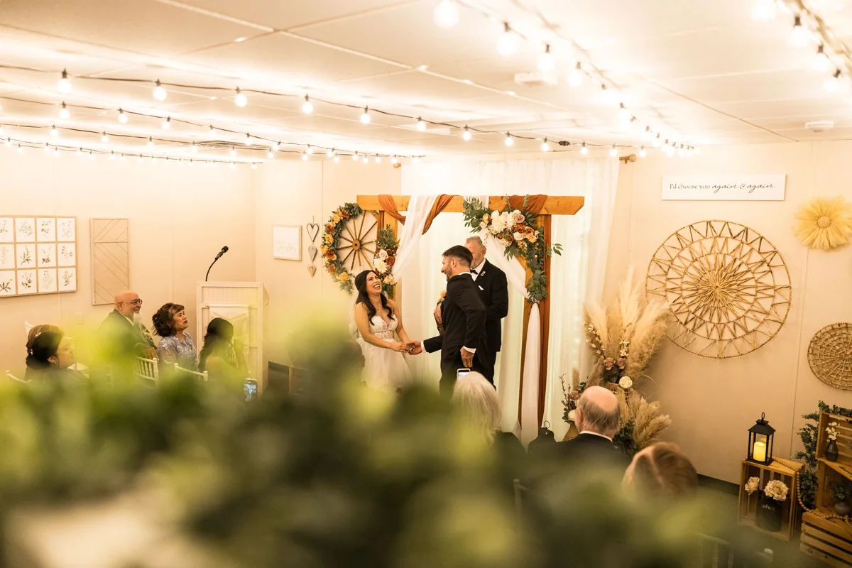 A couple exchanging vows under the floral arch, with their guests looking on.